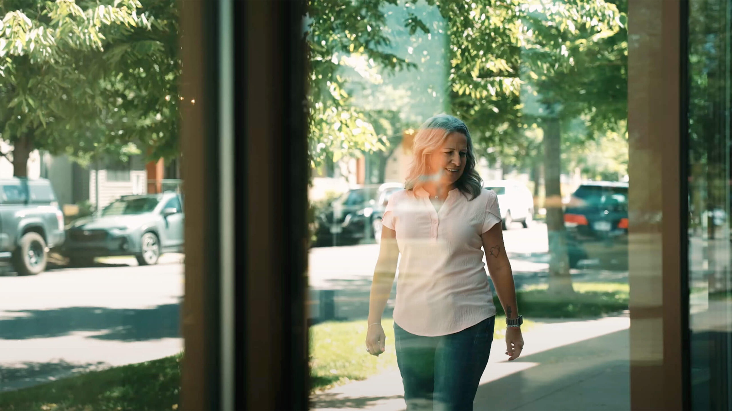 A female breast cancer survivor is walking outside. The picture is taken behind a window showing her healthy and smiling following a breast cancer diagnosis and mastectomy.